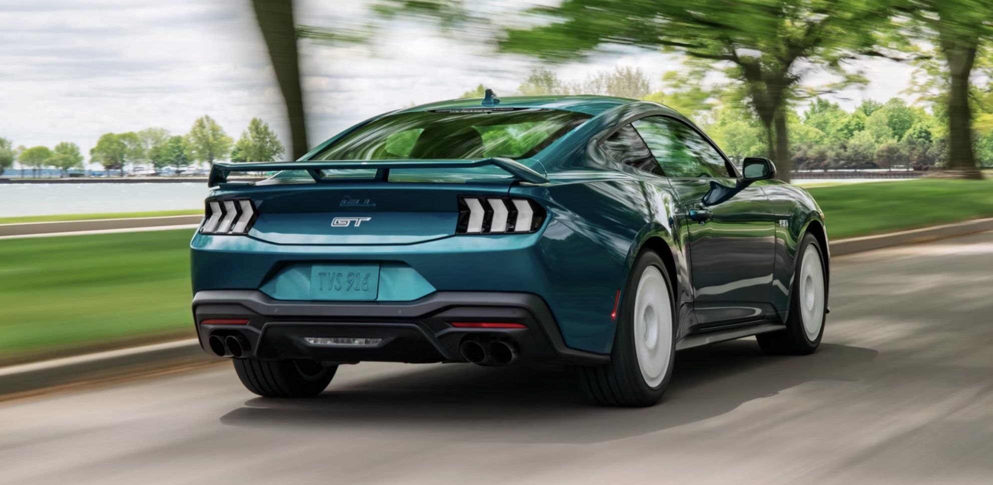 The new 2026 Ford Mustang GT driving down a road in a local Charleston, WV neighborhood with tree cover overhead.